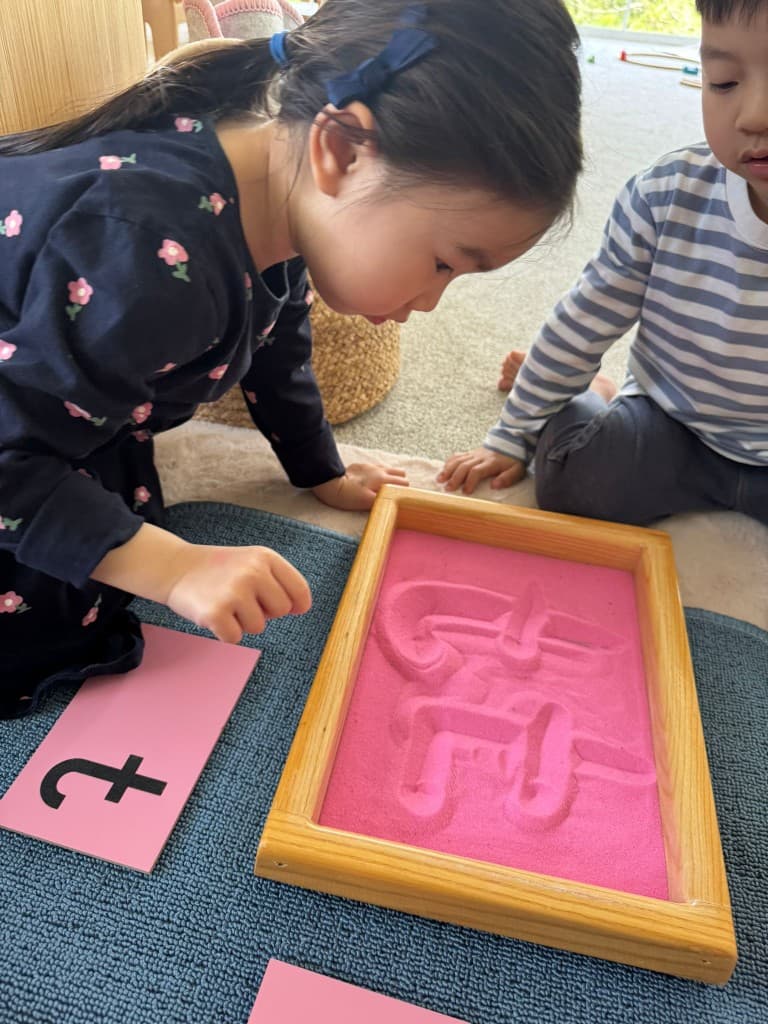 Children tracing letters in sand tray with sandpaper letters